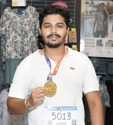 Holding up a gold finisher medal, bib still on